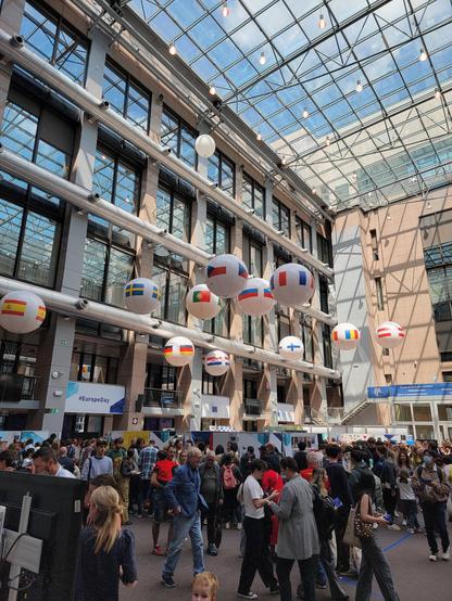 Packed crowd in the big Council atrium, with floating balloons with flags indicating country booths.