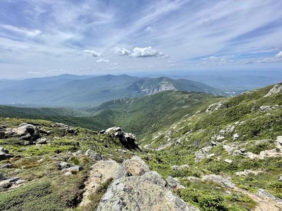 A view hiking  Franconia Ridge in NewHampshire in 2021 with son, just before making it up to Lafayette and turning onto the Greenleaf trail. In the mid distance you see a rocky faced mountain, which is Cannon, a ski slope on the north face. Before that, along the top of a rise is the AMC Greenleaf Hut where you decide to continue north on the Greenleaf trail or left on the Old Bridle Path back to the Falling Waters Trail we began on and to our camp ground on other side of the highway. High, thin clouds are letting through patches of blue on this sunny, comfortably warm day.