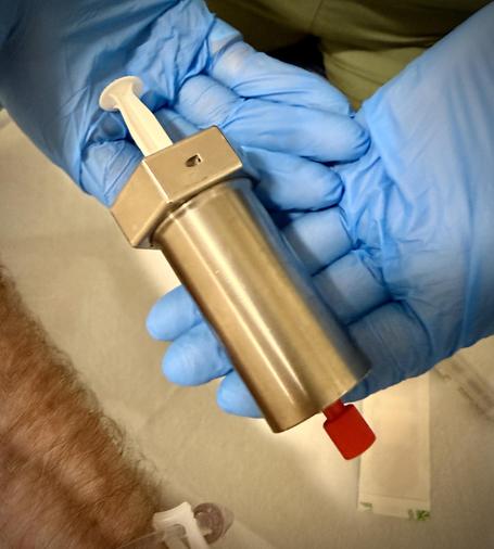 A lead lined metal shield encasing a syringe that holds a radioactive injection for a PET scan in an hour.