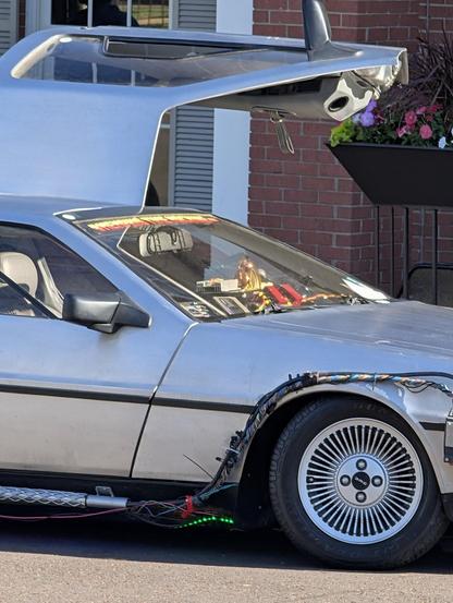 A close up shot of a DeLorean modified to look like the Time Machine from Back To The Future. Its driver side gull wing door is lifted up.