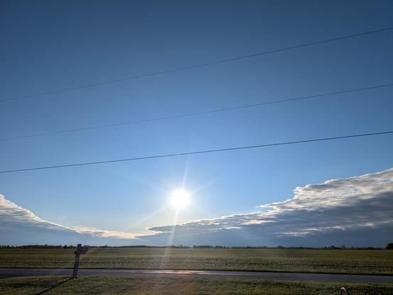 Sunrise over the corn field. The sun is a little farther up than your usual picture, it was cloudy this morning. A bright white ball sits above retreating clouds, dark gray with bright silver edges. Clear and pale blue above.