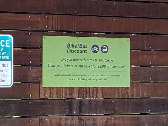 A green sign in the wooden bus shelter, "Bike/Bus Discount" offering discounted zoo admission.