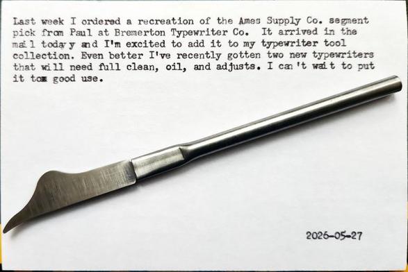 A pen-sized typewriter segment pick with a curved-shaped tip at the end of a thin metal shaft. It sits on top of a typewritten index card that reads: Last week I ordered a recreation of the Ames Supply Co. segment pick from Paul at Bremerton Typewriter Co.  It arrived in the mail today and I'm excited to add it to my typewriter tool collection. Even better, I've recently gotten two new typewriters that will need full clean, oil, and adjusts. I can't wait to put it to good use.