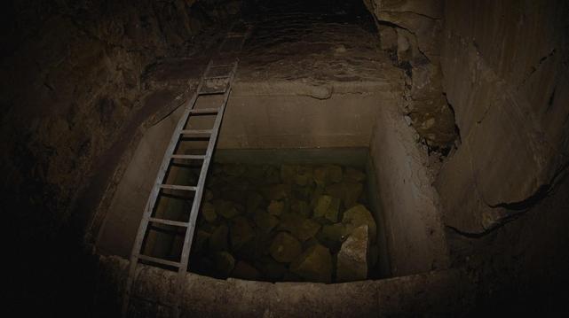 An underground archeological excavation with a ladder and rocks