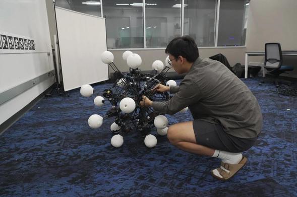 A human adjusting a robot that looks like a supersized virus, with balls on the end of each of 20 omnidirectional legs