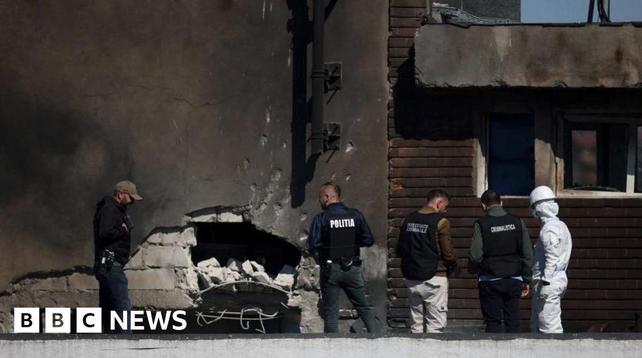 People standing around a building damaged by an explosion