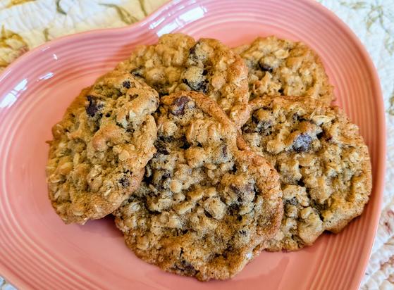 Five chocolate chip and oatmeal cookies on a pink heart shaped plate.