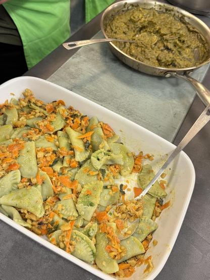 Grüne Ravioli mit Gemüse und Kernen in einer Auflaufform; daneben eine Pfanne mit grüner cremiger Sauce.