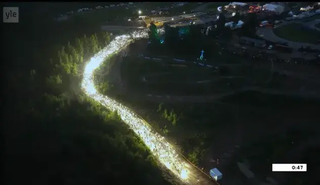 Hundreds of meters long line of light in the darkness of summer evening going through a path into the forest, shot from high above.