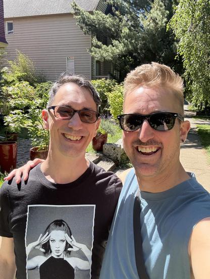 Two tall men pose for a selfie on a sidewalk with sunny weather