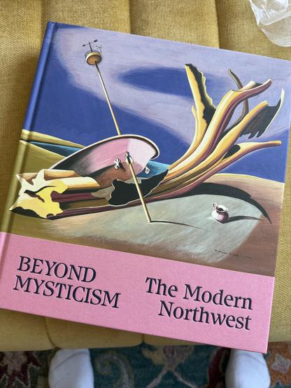A book entitled Beyond Mysticism: The Modern Northwest sits tilted on an upholstered ottoman