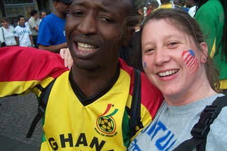 A man wearing a Ghana shirt and a woman wearing a kentucky shirt smile for a selfie.