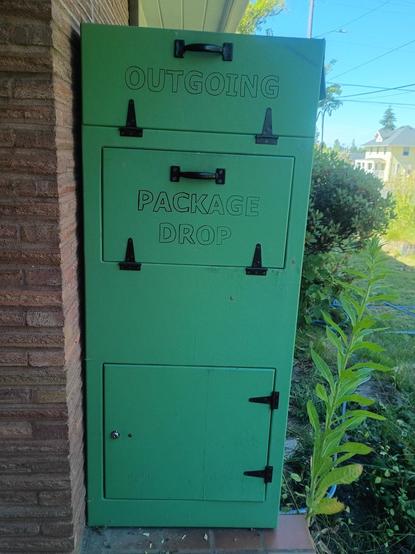 A large wooden box with three doors. The top says "Outgoing". The second to the top says "package drop". The third is at the bottom of the box and has no label, but has a lock that needs a key.