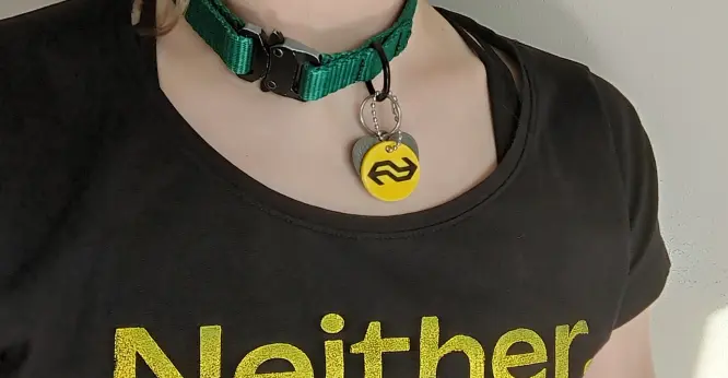 foto van een persoon met een halsband om, aan de halsband is een tag gele bevestigd met het NS-logo