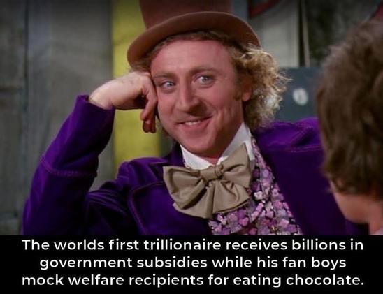 image of the classic "Condescending Wonka" meme featuring actor Gene Wilder as Willy Wonka from the 1971 film Willy Wonka & the Chocolate Factory. He is wearing his signature purple velvet jacket, a floral shirt, a large tan bow tie, and a brown top hat, resting his head on his hand with a smug, patronizing smile as he listens to someone off-camera. Overlaid along the bottom of the image is white text that reads: "The worlds first trillionaire receives billions in government subsidies while his fan boys mock welfare recipients for eating chocolate."