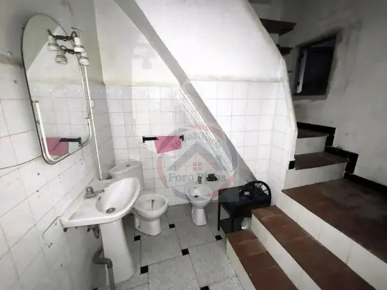Foto de la misma habitación desde otro ángulo donde se puede ver mejor las escaleras, un bidé que no se apreciaba en la otra foto, una mesita y una ventanilla en un descansillo de la escalera.