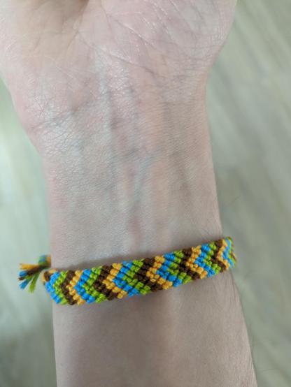a friendship bracelet in chevron pattern wrapped around a wrist. the colors are blue, orange, brown, and green.