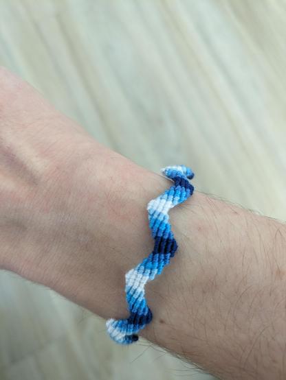 a sine-wave-shaped friendship bracelet wrapped around a wrist. the colors are very dark blue, dark blue, blue, light blue, and white.