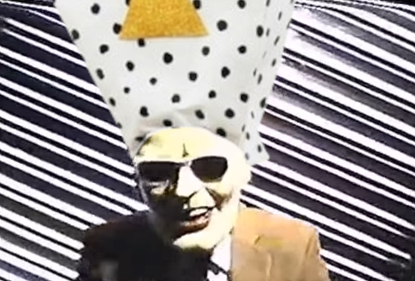 Oh hello viewer of the descriptive text; indeed the answer to the jokes IS in here. This is a collage of a screen capture from the Max Headroom signal hijackings (in Chicago, November 1987), wearing the hat of Khn de Poitrine, current triangle band microtonal celebrity.