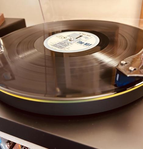 A close-up of a spinning vinyl record on a turntable with a partially visible colorful label.