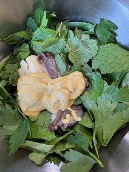 Basil, mint and parsley in a steel mixing bowl with mustard, anchovies and garlic.