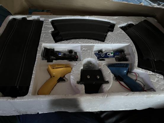 The inside of a Scaletrix box showing lots of track, a yellow and blue controller, power supply and two cars
