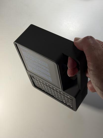 A hand holding a small grey plastic computer by the handle.