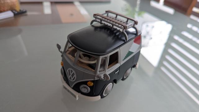 A tiny black classic VW Bus from Playmobil. It has the colors of the Mexican flag painted on the side.