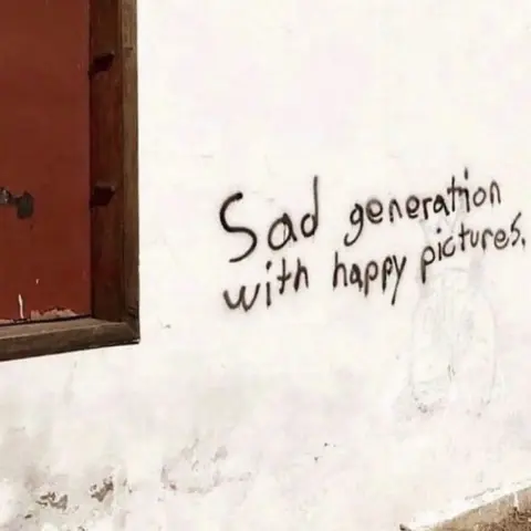 Some graffiti sprayed on a white wall saying "Sad generation with happy pictures".