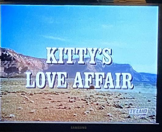 A screen capture of the title of a television show. The capture shows a desert scene, with text in the middle of the image that says “Kitty‘s Love Affair”.