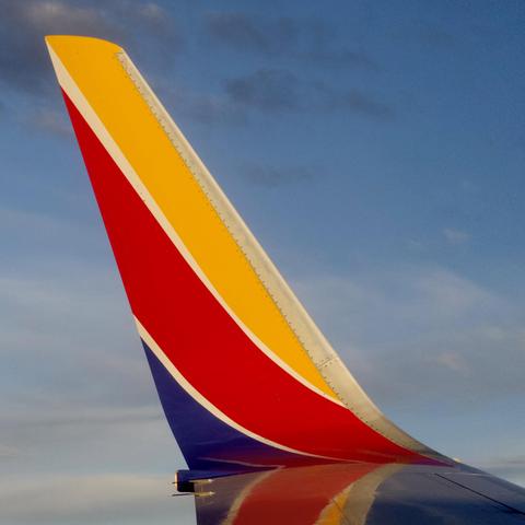 A Southwest Airlines airplane tail fin against a blue sky, displaying the airline's distinctive livery of red, gold, and blue colors with white trim.