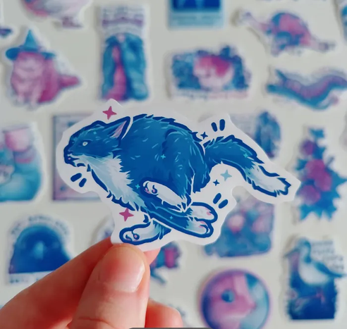 Hand holding up a sticker of a tuxedo cat having zoomies