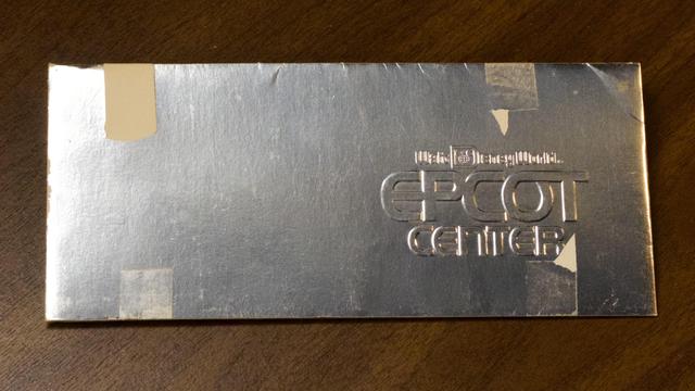 A silver foil envelope embossed with Walt Disney World EPCOT Center, shown from above on a wooden surface.