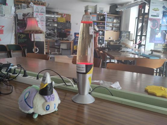 a plush möth wearing one of those lava lamp cones as a hat, there is also a lava lamp to the side