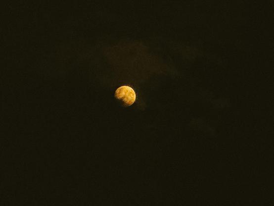 a nearly full moon partially covered by clouds. The moon is very golden in hue.