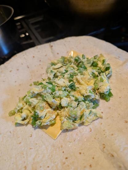 A tortilla with 2 slices American cheese and 2 eggs scrambled with 1 while bunch of chopped green onions
