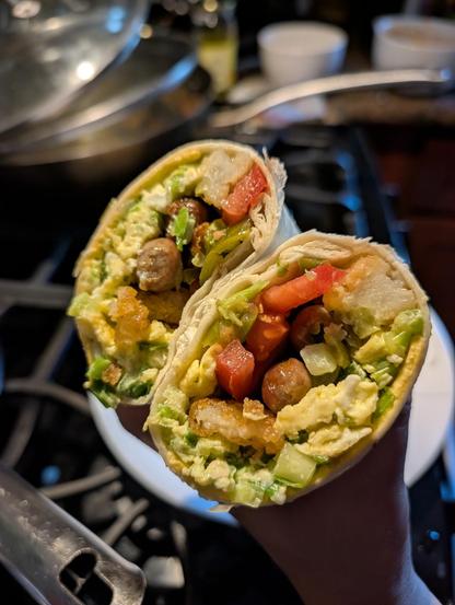 A sliced crossed section of a breakfast burrito with eggs, scallions, tomato, tater tots, pickled jalapeno, sausage