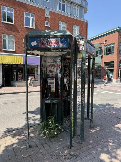 two very wrecked telephone booths covered in graffiti and stickers