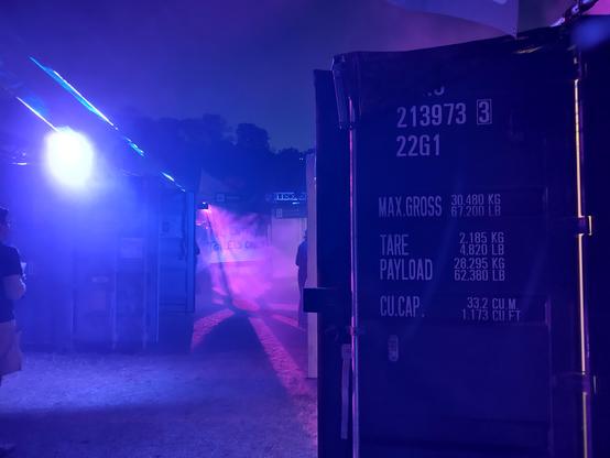 #nullsector at night, in purple & blue light, a container door in the front, shadowy figure in the back.