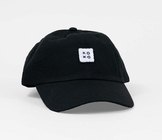 Photo of a black baseball cap with a square white felt logo sewn with the letters “XOXO” in the center