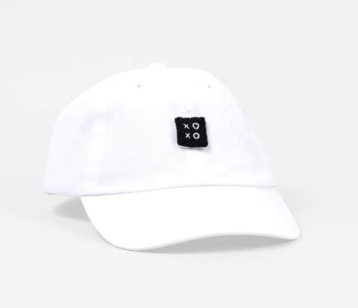 Photo of a white baseball cap with a square black felt logo sewn with the letters “XOXO” in the center