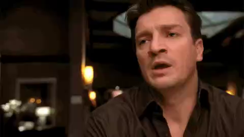 Nathan Fillion raises hand and moves mouth to start speaking but stops himself, tries a second time with a second subtle hand movement, but stops again before being able to say anything. Instead, gives up, looks down and rests his face on his hand.