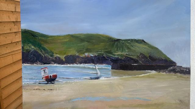 A landscape painting featuring a beach scene with two boats, one in the foreground (a red and white boat) and another small sailing boat along in the water. The background includes green hills and a rocky shore under a blue sky. The left side shows a wooden fence.