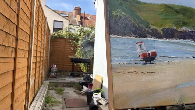 A partially visible painting of a red and white boat on a beach, set against a backdrop of hills and blue water. The background features a garden area with a wooden fence, a lit grill with some smoke, and some scattered items.