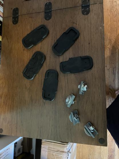 Five black rubber pads with grippy bottoms and four bits of metal with nuts and bolts.