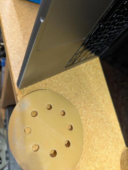 a loose sanding disk (meant for a handheld oscillating sander) on the garage workbench with a spot of silvery dust on one edge, below my aluminum laptop propped open so as to stand up sideways while I work on it
