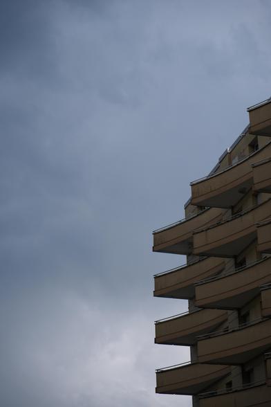 triangular, gently curved balconies protruding from a dark, yellow building, photographed in front of overcast skies