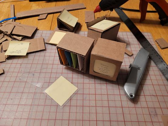 Cutting mat with cardboard pieces and a bunch of cubic projects involving sticky notes.