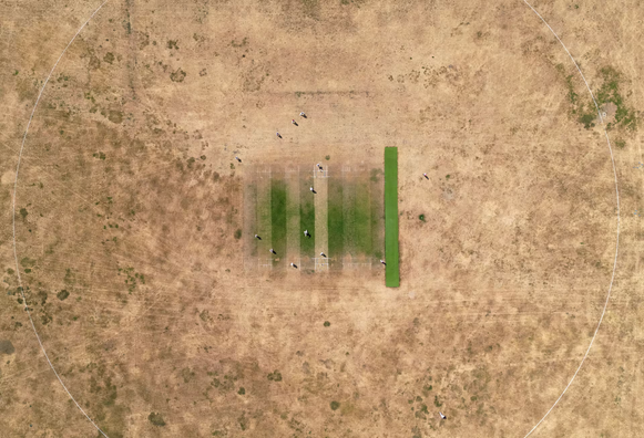 A drone view shows players taking part in a local cricket match playing on a pitch surrounded by parched grassland,