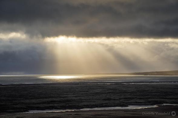 Moody view. Massive clouds over the sea, a gap through which sun rays are beaming down. Some land in the distance and in the front.